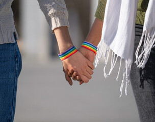 Close up of lesbian couple holding hands wearing rainbow bracelets: celebrating lgbtq+ pride and...