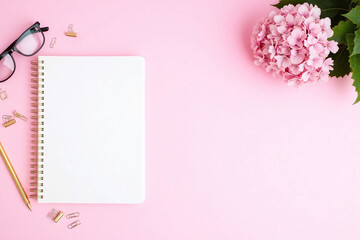 notebook with a pen glasses and a flower on a pink background