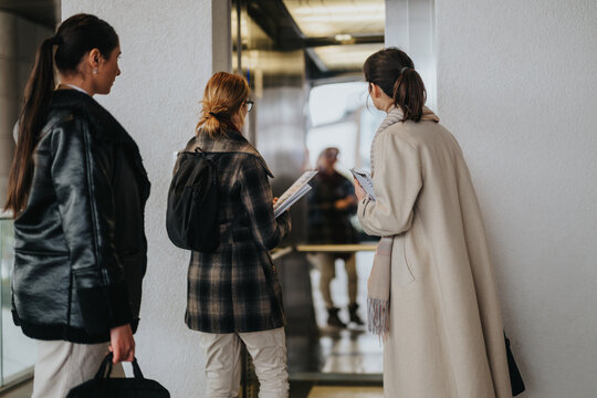 A group of professional women standing near an elevator, appearing focused and prepared.