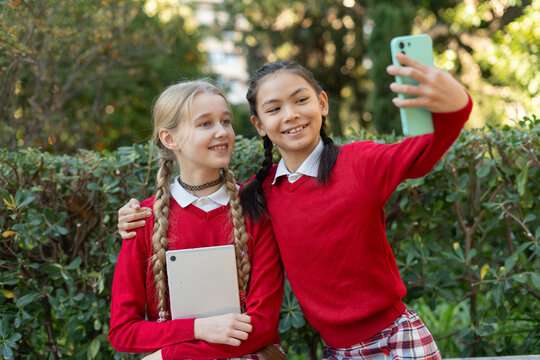 Two smiling students taking a selfie with smartphone outdoors