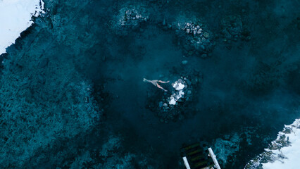 Aerial view of a lone woman relaxing in a stunning thermal spring surrounded by snowy landscapes in...