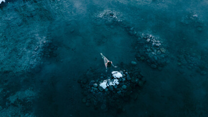 Aerial view of a lone woman relaxing in a stunning thermal spring surrounded by snowy landscapes in...