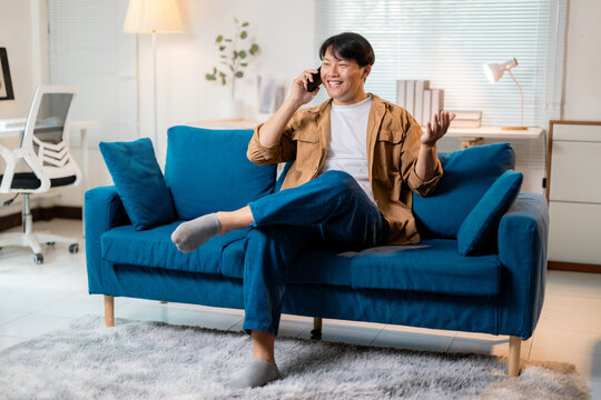Happy young man using smartphone while relaxing on comfortable sofa at home