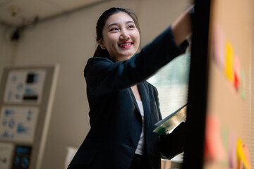 Smiling businesswoman holding documents and attaching sticky notes to a whiteboard during a meeting...