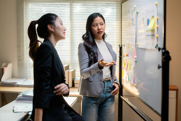 Two businesswomen are discussing and brainstorming using sticky notes on whiteboard in modern office