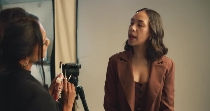 Studio, makeup artist and women on set, model and preparing for photoshoot, glow and cosmetics. Production, lipstick and makeover for girl with brush, behind the scenes and people with equipment