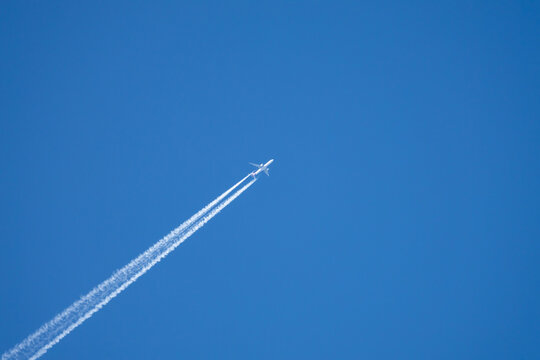 Airplane in a blue sky without clouds. The airplane has a flight trail behind it.