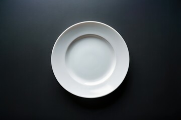 Clean, empty white ceramic plate, isolated on black. Overhead studio shot; minimalist food photography prop.