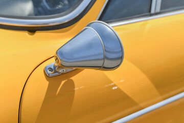 Close up yellow vintage car chrome rusty rearview side mirror