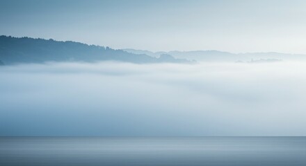 Fototapeta premium A serene landscape of misty hills blending into a calm water surface.