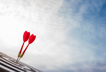 Two red darts hitting the bullseye on a target board under a bright sky. Symbol of accuracy, success, achievement, and goal setting in business, sports, and personal growth.
