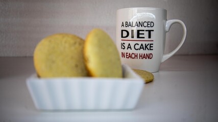 A white ceramic mug with a humorous quote about dieting sits behind a plate of golden, homemade cookies.