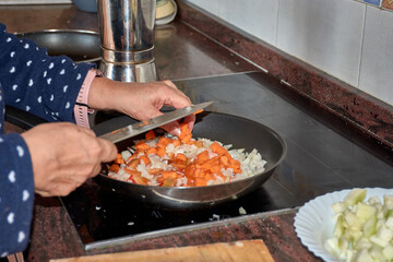 Person carefully slicing vegetables and dropping them into a pan for a homemade dish