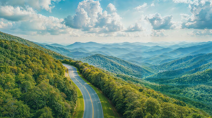 Aerial View of Winding Mountain Road Through Lush Green Forests Under Blue Sky