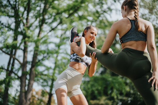 Two women engage in partner stretching exercises outdoors in a scenic park environment, emphasizing physical fitness, teamwork, and an active lifestyle.
