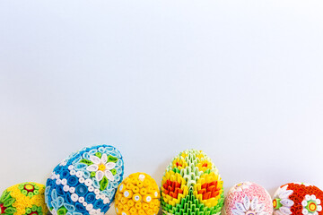 White Easter background with colorful Easter eggs with floral ornaments and origami decorations at the bottom, copy space.