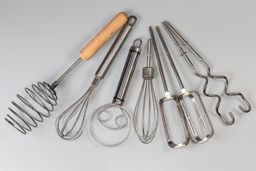 Different hand kitchen whisks and mixer attachments on gray background