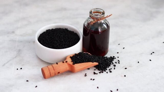 Black Seed in White Bowl, Black  Seed Oil in Glass Bottle, and Wooden Scoop of black seeds, Transition from Left to Right