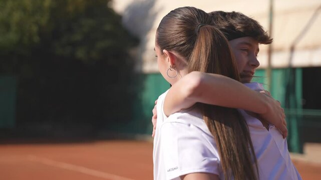 After playing tennis, a couple of teenage tennis players shake hands and give each other a high-five on the net..