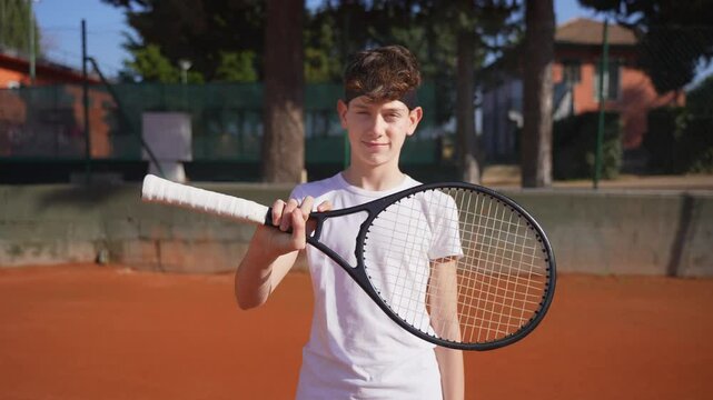 A teenage tennis player worming his wrist before a tennis workout or a competition, looking at the camera and smiling.
