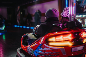A couple enjoying a ride together in a red bumper car surrounded by vibrant colorful neon lights...