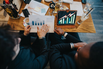 Two colleagues in a meeting analyzing business data with graphs, charts, and a tablet display in a collaborative office environment.