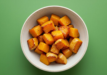 Roasted Butternut Squash Cubes in a White Bowl Against a Green Background
