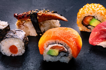 Sushi rolls on a black background. Uramaki with salmon, avocado, and cream cheese, eel sushi and other rolls and maki