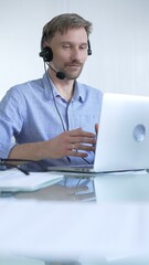 Male office worker demonstrates the significance of technology in modern business through client communication using laptop and headset. Business people concept