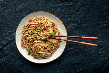 Soba, Japanese buckwheat noodles, boiled, on a plate on a black slate background, with chopsticks, a flat lay
