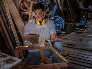 Skilled Carpenter Reviewing Plans and Blueprints in Rustic Wood , Professional Carpenter use tablet  working to making woodcraft furniture in wood workshop 