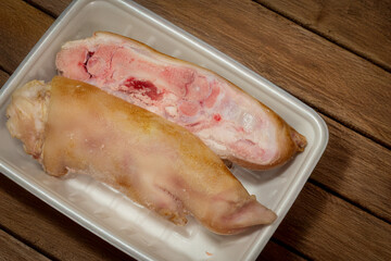 Uncooked pig trotters cut in halves in a styrofoam container from the supermarket on a wooden surface
