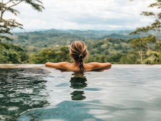 Fototapeta premium Woman relaxing in infinity pool overlooking jungle mountains