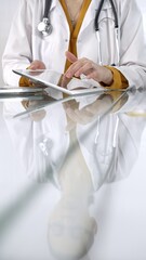 Unknown doctor woman wearing a stethoscope, yellow blouse under a lab coat, is using digital tablet in modern healthcare setting, interacting with patient data, vertical portrait. Medicine concept