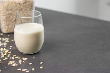 A glass of oat milk and oatmeal in a box on grey kitchen table. Vegan and non-dairy alternative milk