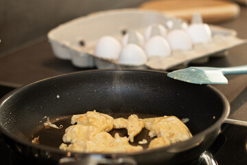 Close up of scrambled omelet egg in a black pan with a blue spatula, blurred background with white eggs 