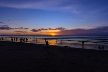beautiful colourful sunset on Kuta Beach on the island of Bali blue purple orange skies with turquoise blue waters and silhouette of people on the sandy beach the land of gods Bali Island Indonesia