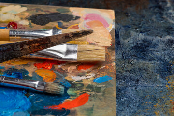 Obraz premium Old used brushes and palette knife in an artist's studio, palette with multi-colored spots of oil or acrylic paint