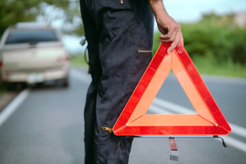Roadside assistance at a vehicle breakdown with warning triangle in hand during daylight