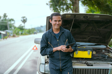 Mechanic checks tablet for information while standing by broken car on roadside during daytime