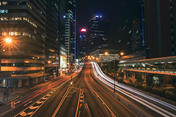 A mesmerizing long exposure photograph of Hong Kong's vibrant cityscape at night. Towering skyscrapers pierce the inky sky, their illuminated windows creating a dazzling tapestry of light. 