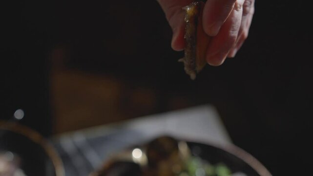 A hand is holding a piece of food that is dripping. The food is likely a type of sauce or condiment, and the dripping suggests that it is being poured or drizzled onto something else