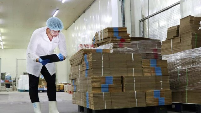 Male store staff packing room sardine canned fish factory check and count cardboard boxes on pallets and put them on a clipboard ensure they are good quality and meet standards packaging product sale.