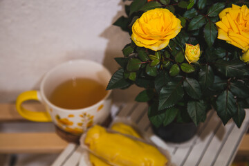 A cup of tea, cakes and blooming yellow roses on a wooden table