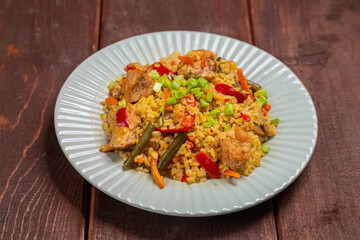 On a wooden table in a plate there are vegetables stewed with bulgur