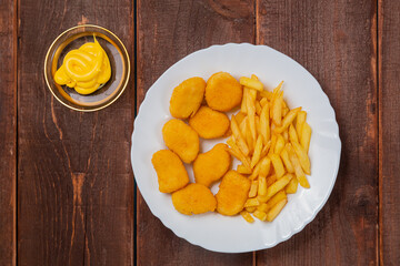 French fries and golden chicken nuggets in a plate next to cheese sauce