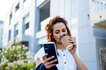 Businesswoman drinking coffee and using smartphone in urban setting