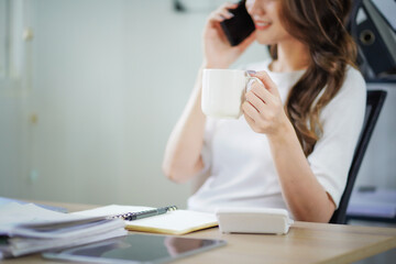 A woman is talking on her cell phone while holding a white coffee cup