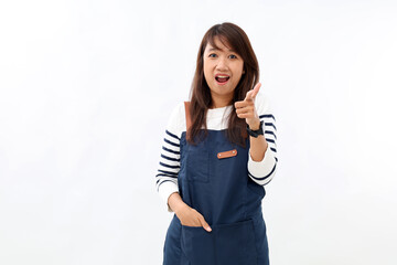 Naklejka premium Beautiful asian barista in blue apron welcome guests to coffee shop, pointing finger gun, standing against white background
