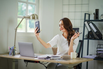 A woman is sitting at a desk with a laptop and a cell phone